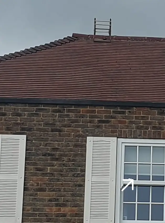 Brick house with white window shutters and a roof ladder extending above the red tiled roof.