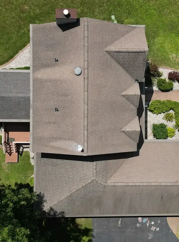 Aerial view of a house roof with multiple gables, chimneys, surrounded by green lawn and garden.