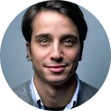 Portrait of a man with dark hair wearing a gray sweater over a blue collared shirt.