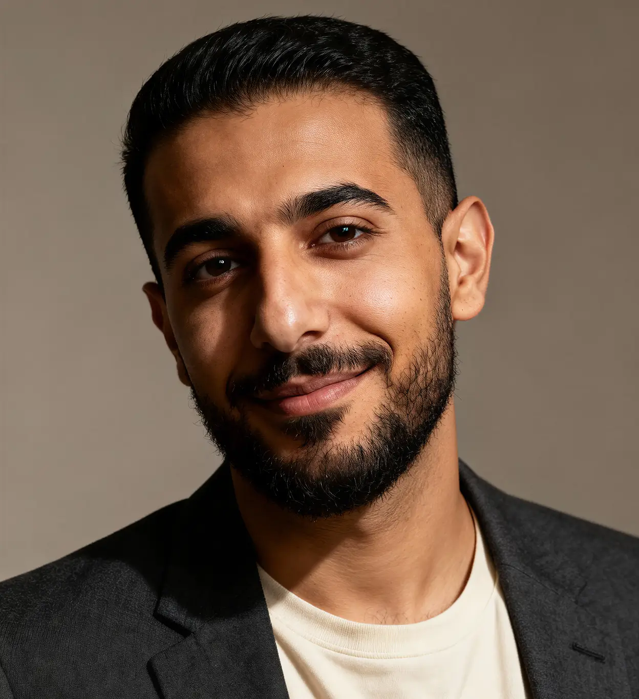 Smiling young man with short black hair and beard, wearing a black jacket and cream shirt.