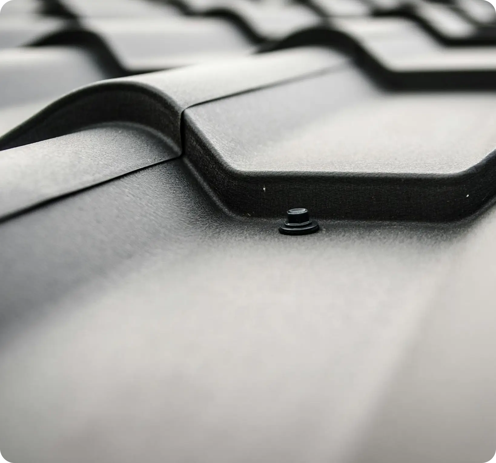 Close-up of dark textured interlocking roof tiles with a black screw at the center.